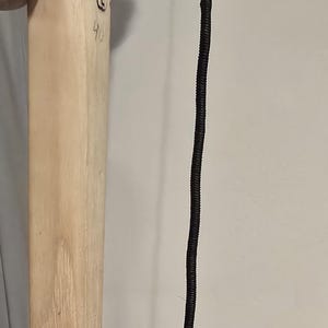 Może przedstawiać: Zbliżenie drewnianego kołka z czarnym oznaczeniem i numerem 40. Czarna, ciasno zwinięta lina wisi obok kołka. Lina jest przymocowana do cieńszej, beżowej liny.