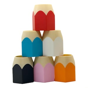 May include: A pyramid of six pencil-shaped containers in red, blue, white, black, pink, and orange. Each container has a beige top, resembling a pencil eraser, and a hexagonal body.