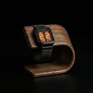 May include: A black digital watch with an orange display rests on a curved wooden stand. The watch has a rectangular face and a mesh band. The stand is made of dark wood and has a smooth, polished finish.