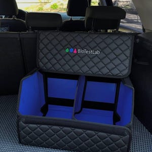 May include: Black quilted car organizer with blue interior compartments. The organizer has a lid and is designed to fit in the trunk of a car. The text "BioTestLab" is visible on the lid.