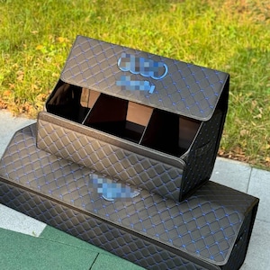 以下が含まれることがあります： 青いステッチとダイヤモンド模様が施された黒い車のトランクオーガナイザー。 オーガナイザーには複数のコンパートメントと蓋があります。 ロゴは蓋に表示されます。 車のトランクを整理するように設計されています。