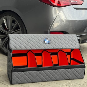 Puede incluir: Organizador de maletero de coche acolchado gris con ribete negro y compartimentos interiores naranjas. Cuenta con un logotipo de BMW en la tapa. Dise&ntilde;ado para mantener el maletero ordenado.