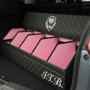May include: Black quilted car trunk organizer with pink interior compartments. Features a white lion emblem and the initials "J.T.B." in script. The organizer is designed to fit in the trunk of a vehicle.