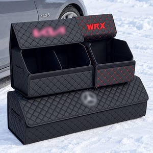 May include: A black car trunk organizer set featuring a quilted diamond pattern with red stitching. The set includes a large rectangular base bin and two smaller upper compartments, one of which displays the red embroidered text WRX.
