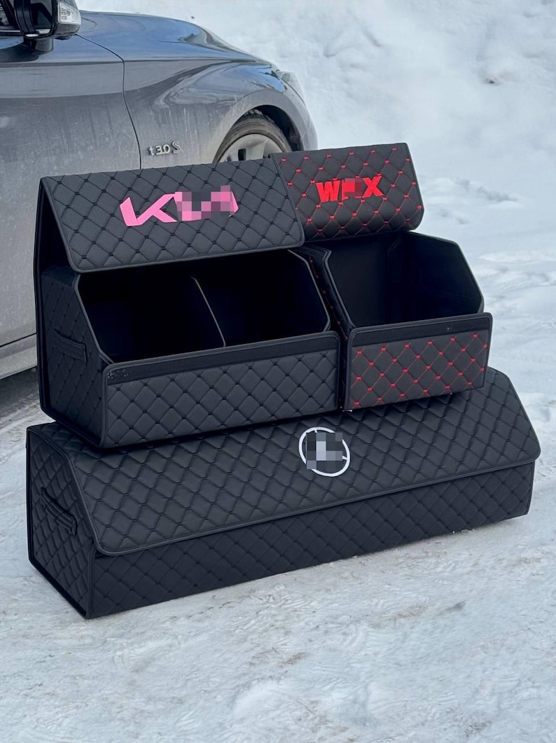 May include: Black quilted car trunk organizers with pink and red text accents. The organizers are stacked, featuring multiple compartments and a logo. The design includes a diamond pattern.