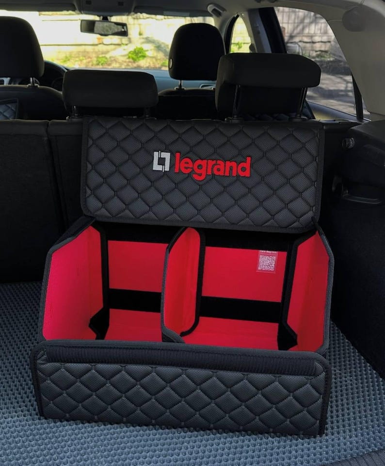 以下が含まれることがあります： 「Legrand」のロゴが入った黒と赤の車のトランクオーガナイザー。オーガナイザーの外側はキルティング模様で、赤い内装の2つのコンパートメントがあります。車の後部に収まるように設計されています。