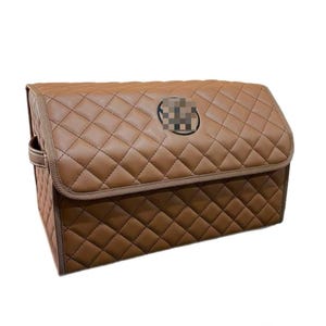 May include: Brown quilted car organizer with a diamond pattern. The organizer has a rectangular shape with a lid and a handle on the side. A circular emblem is on the front.