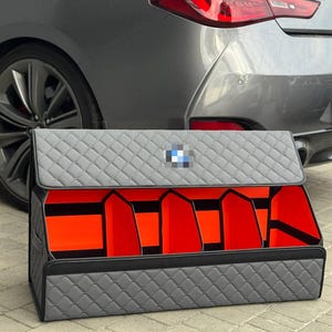 Może przedstawiać: Szary pikowany organizer do bagażnika samochodowego z czarnym wykończeniem i pomarańczowymi przegrodami wewnętrznymi. Posiada logo BMW na pokrywie. Zaprojektowany, aby utrzymać bagażnik samochodu w porządku.