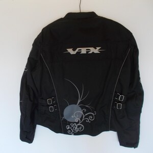 May include: Black motorcycle jacket with the text "VFX" in silver across the back. The jacket has silver accents, a decorative design, and two sets of buckles on the lower back.