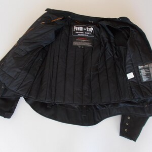 May include: Black motorcycle jacket with the interior visible. The jacket has a quilted lining and multiple pockets. The "Power-Trip" logo is visible on the chest. The sleeves have button details.