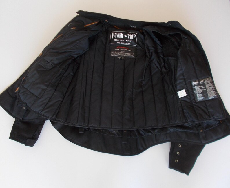 May include: Black motorcycle jacket with the interior visible. The jacket has a quilted lining and multiple pockets. The "Power-Trip" logo is visible on the chest. The sleeves have button details.