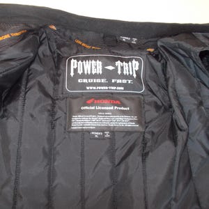 May include: Black motorcycle jacket interior with quilted lining. Features a Power Trip label with "Cruise. Fast." text and a Honda official licensed product label. The jacket has a Women's XL size tag.