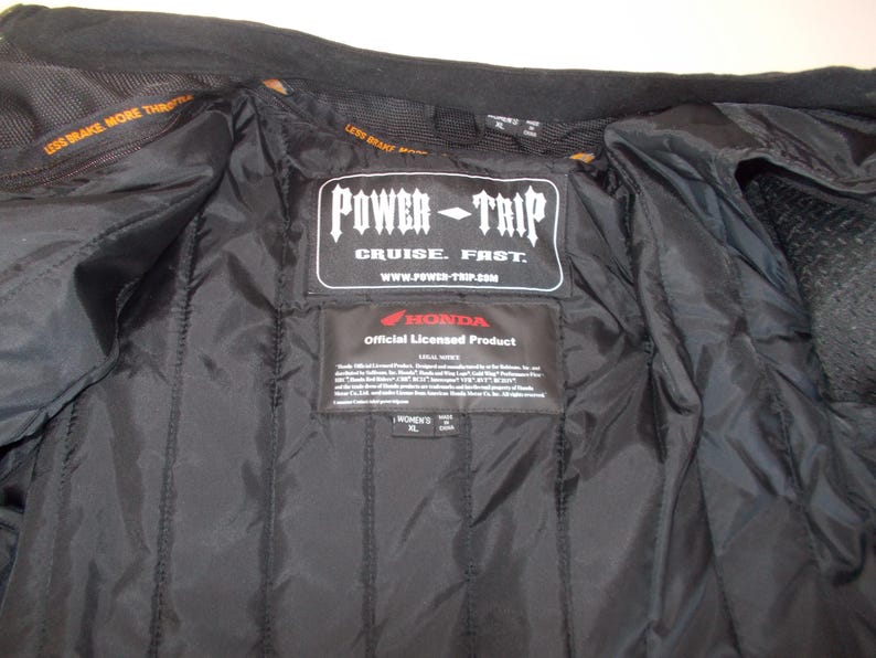 May include: Black motorcycle jacket interior with quilted lining. Features a Power Trip label with "Cruise. Fast." text and a Honda official licensed product label. The jacket has a Women's XL size tag.