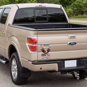 May include: A tan Ford F-150 truck with a sticker featuring an eagle, the American flag, and the text "Family and Flag." The truck has black tires and a Ford emblem.