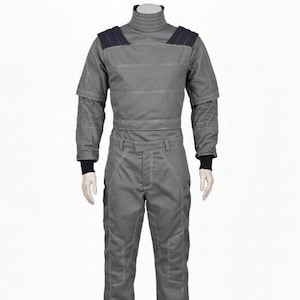 Op de afbeelding: Een grijze jumpsuit met een hoge kraag en donkerblauwe schouderaccenten. Het eendelige kledingstuk heeft witte stiksels, lange mouwen en zwarte manchetten. De broek heeft zakken en een bijpassend wit stikselontwerp.