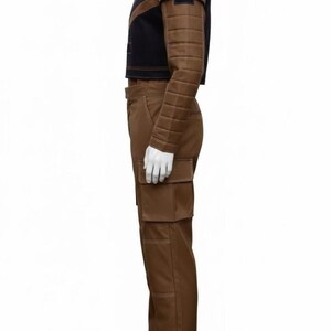May include: A brown and black outfit consisting of a cropped jacket and pants. The jacket has quilted sleeves and shoulder accents. The pants have large pockets. The outfit is displayed on a mannequin.