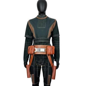 May include: A dark green long-sleeved jumpsuit featuring light brown paneling, vertical stitching, and a brown utility belt with two side pouches and a central metallic buckle. The outfit includes two long brown holsters hanging from the belt.