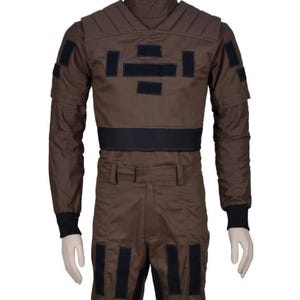 May include: Brown jumpsuit with black accents, featuring a high collar and multiple rectangular patches. The long-sleeved top has a padded chest and shoulders, with black cuffs at the wrists. The pants have matching black patches.