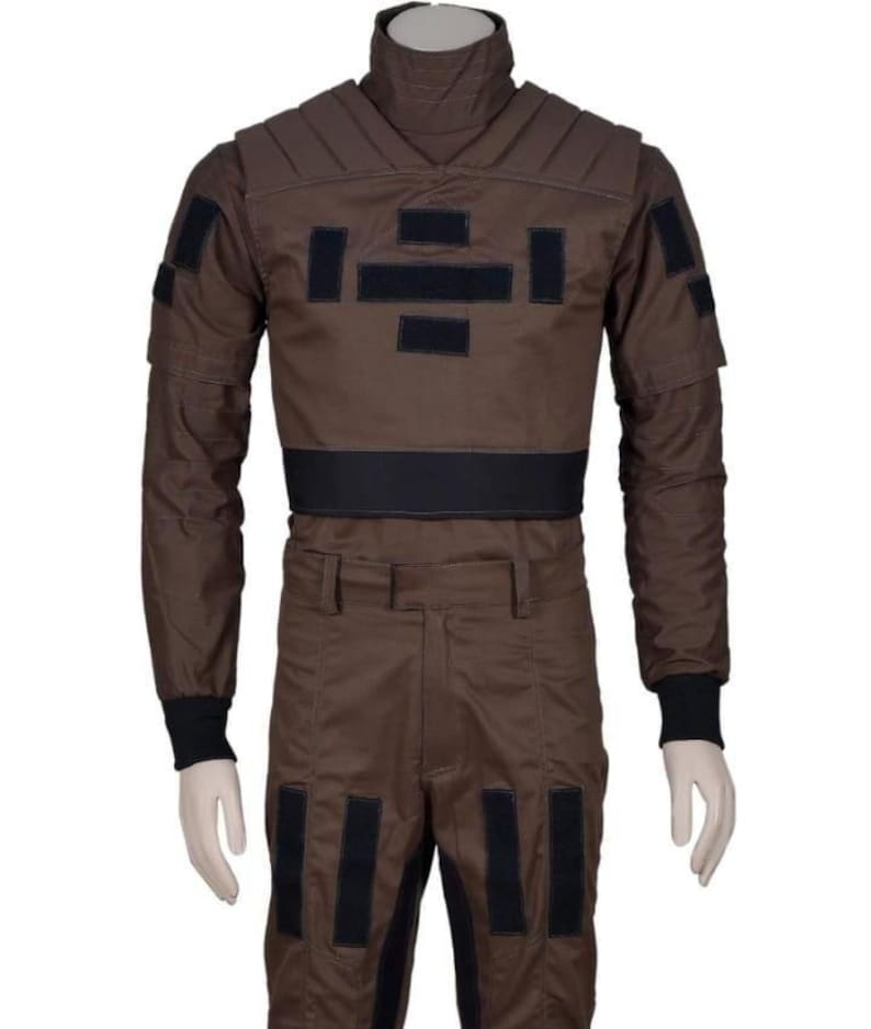 May include: Brown jumpsuit with black accents, featuring a high collar and multiple rectangular patches. The long-sleeved top has a padded chest and shoulders, with black cuffs at the wrists. The pants have matching black patches.