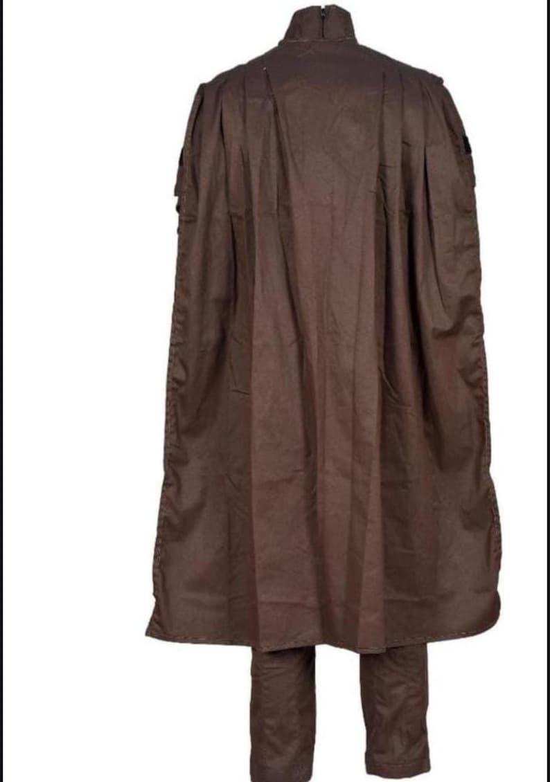 May include: A brown outfit consisting of a long cape and matching pants. The cape has a high collar and extends to the knees. The pants are straight-legged. The outfit is made of a solid, matte fabric.