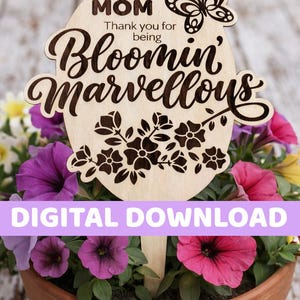 Puede incluir: Una estaca de jardín de madera con las palabras "MOM Thank you for being Bloomin' Marvellous" y un diseño de mariposa y flores. La estaca está colocada en una maceta de terracota llena de flores moradas, rosas y amarillas. Las palabras "DIGITAL DOWNLOAD" se muestran en una pancarta morada.