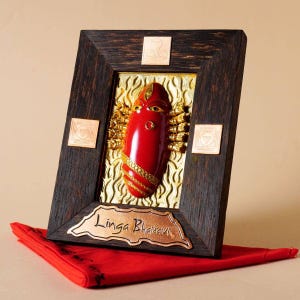 Puede incluir: Una obra de arte religiosa enmarcada que presenta una deidad roja estilizada con detalles dorados. La obra de arte está sobre un fondo dorado dentro de un marco de madera oscura. El texto "Linga Bharavi" se muestra en una placa color cobre.