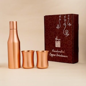 May include: A copper-coloured drinkware set featuring a bottle and two cups, presented with a decorative box. The bottle has a slender design with a cap. The cups have a curved shape. The box is dark red with white floral patterns and the text "Handcrafted Copper Drinkware."