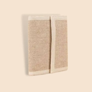 Puede incluir: Una cartera beige tejida con un borde color crema. La cartera rectangular está hecha de una tela texturizada. El borde crema enmarca el material tejido, creando un diseño simple y neutro.