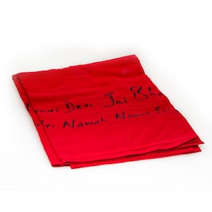 Puede incluir: Un paño rojo brillante doblado con texto manuscrito negro. El texto parece ser una frase religiosa. El paño está cuidadosamente doblado y parece estar hecho de un material suave.