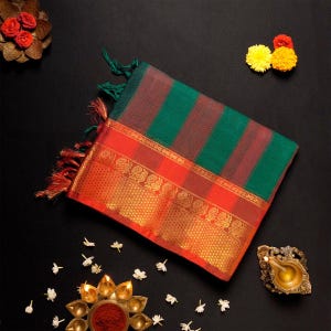 May include: A colourful textile featuring green and red stripes, with an orange border adorned with gold floral patterns. The fabric has decorative tassels at the ends. The image is set against a black background with floral and decorative elements.