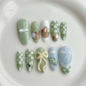 以下が含まれることがあります： ピクニックをテーマにした10本のつけ爪のセット。ピクニックバスケット、ギンガムチェック柄、リボン、凧のデザインが特徴です。カラーパレットは、緑、白、水色の色合いで、気まぐれで夏らしい美しさを演出しています。