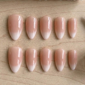 May include: A set of ten press-on nails arranged in two rows of five. Each nail features a smooth, glossy finish with a soft ombre gradient, transitioning from a natural nude pink at the base to a crisp white tip in an almond-shaped silhouette.