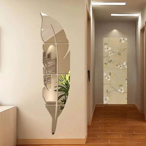 以下が含まれることがあります： ベージュの壁に取り付けられた、大きな鏡面フェザーウォールデコレーション。 羽根はいくつかの部分に分かれており、周囲の部屋を映し出しています。 この装飾は、空間にモダンで芸術的なタッチを加えます。