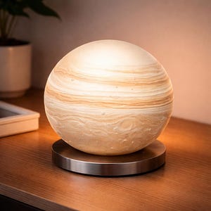 May include: A spherical lamp with a planet-like design, featuring swirling bands of beige and white. The lamp sits on a round, brushed metal base. The lamp is a decorative lighting fixture.
