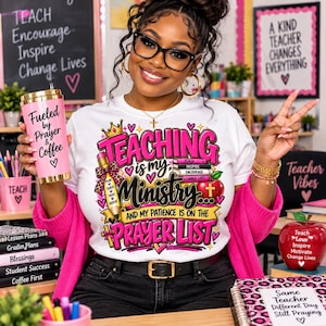 May include: A white t-shirt featuring a graphic with the text Teaching is my Ministry and my patience is on the prayer list, decorated with a crown, pencil, books, and apple. The shirt is paired with a pink tumbler labeled Fueled by Prayer & Coffee.