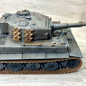 May include: A detailed model of a military tank, primarily gray with brown and gold accents. The tank features a long gun barrel and intricate track detailing. The model appears to be a replica of a historical armored vehicle.