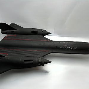 Puede incluir: Un modelo de avión negro con líneas rojas y el texto "U.S. AIR FORCE". El modelo tiene un diseño elegante con dos motores y una nariz puntiaguda. Las alas están inclinadas hacia arriba.