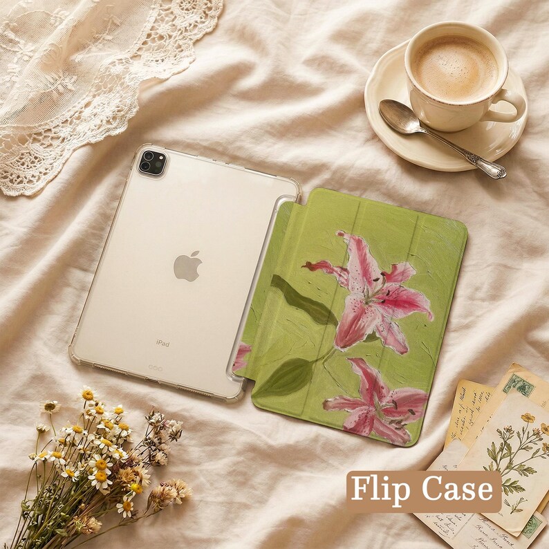 May include: A tablet flip case featuring a green background with a painted pink lily design. The case is open, revealing a silver tablet with a clear protective shell. The text "Flip Case" is printed in a brown box in the bottom right corner.