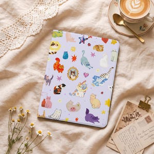 Puede incluir: Una funda rectangular para tableta con fondo lavanda claro que presenta un patrón repetitivo de varios gatos ilustrados en diferentes colores y posturas, intercalados con pequeñas estrellas, corazones, flores de colores y un retrato de gato enmarcado.