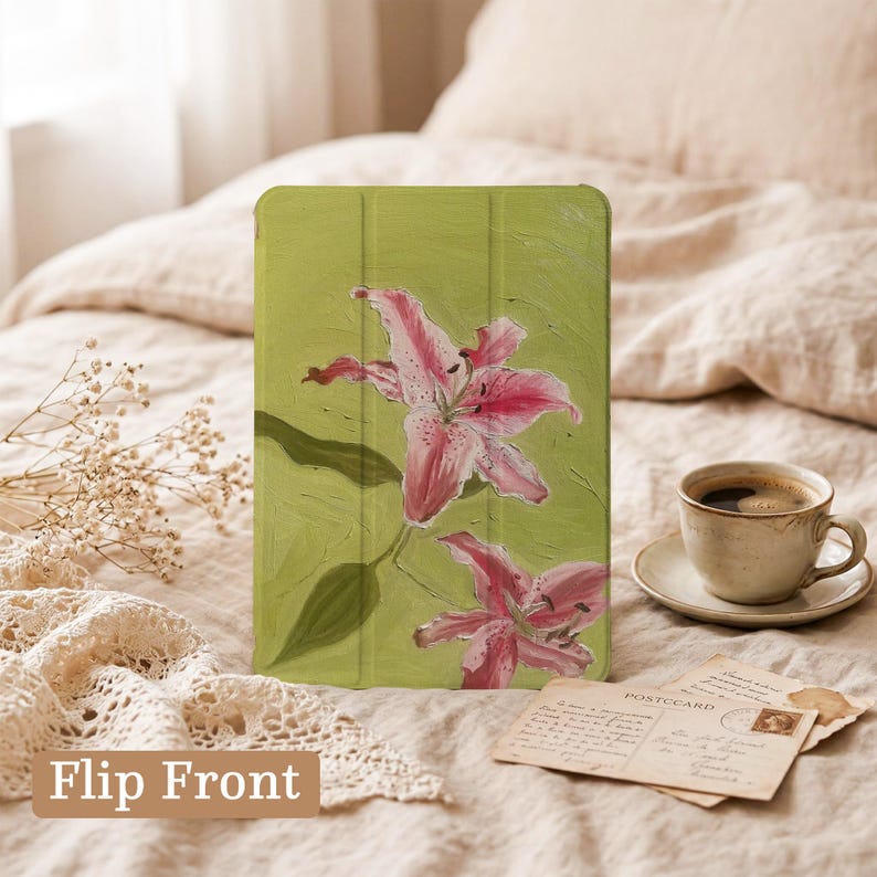 May include: A rectangular tablet case featuring a painted design of two pink lilies on a textured light green background. The case has a tri-fold cover design with visible vertical creases and the text Flip Front printed in the bottom left corner.