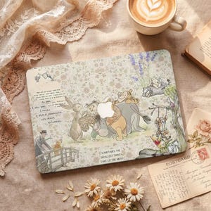 Könnte beinhalten: Eine beige Laptop-Hülle mit einer Illustration von Winnie Puuh und seinen Freunden. Das Design umfasst florale Muster, Text und das Zitat: "Sometimes the smallest things take up the most." Eine Kaffeetasse und eine Postkarte sind ebenfalls zu sehen.