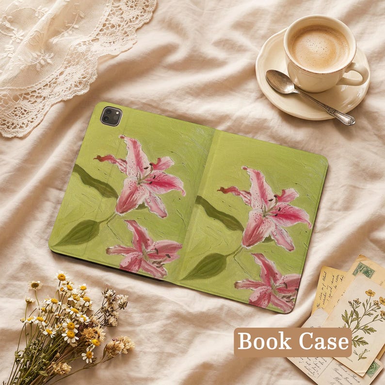 May include: A tablet case featuring a light green background with a painted design of pink lily flowers and green leaves. The case has a rectangular shape with a camera cutout in the top left corner and a textured surface finish.