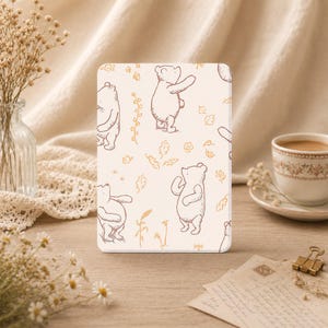 Pode incluir: Uma capa retangular para tablet com fundo creme claro e um padrão repetitivo de linhas castanhas que apresenta uma personagem de urso, pequenas folhas e ramos florais dispostos delicadamente sobre a superfície.