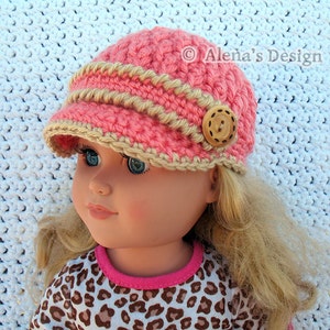 May include: A pink and beige crocheted doll hat with a button on top. The hat has a wide brim and a braided trim.  &copy; Alena's Design