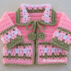 May include: A pink crocheted baby cardigan with green and white trim. The cardigan has a small bow at the neckline and a flower design on the front.