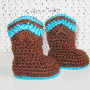 May include: A pair of brown crocheted baby booties with a blue trim. The booties are on a white crocheted surface.