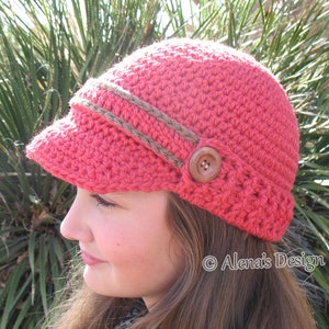 May include: A coral pink crocheted hat with a brown crocheted brim and a brown button. The hat has a slightly slouched look and is worn by a person with long brown hair.