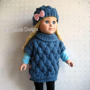 May include: A blue knitted sweater with a cable knit pattern and a turtleneck collar. The sweater has a pink bow on the front and is worn by a doll with blonde hair and blue eyes. The doll is wearing a blue hat with a pink bow.