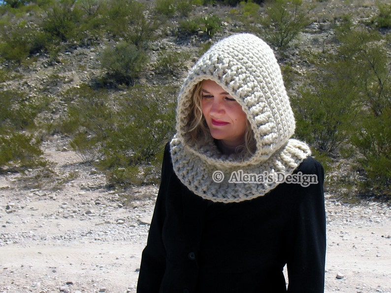 May include: A beige crocheted hood and cowl set. The hood features a ribbed design and a rounded top, connected to a cowl that fits around the neck. The set is made of a thick, textured yarn. The text "Alena's Design" is visible.