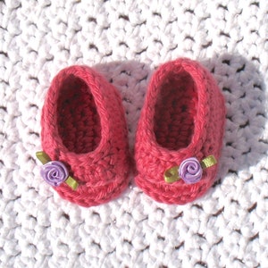K&ouml;nnte beinhalten: Ein Paar rosa geh&auml;kelte Babyschuhe mit lila und gr&uuml;nen Blumenverzierungen.